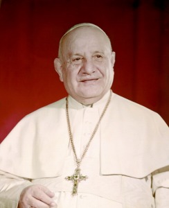 Pope John XXIII smiling and wearing a light coloured pope's dress, a crucifix and a white zucchetto
